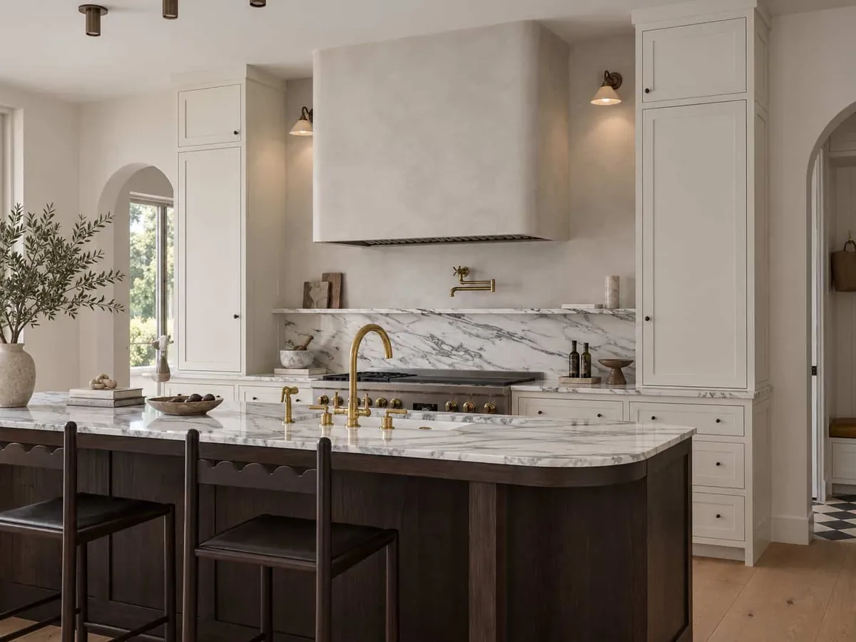 Kitchen range hood in warm white plaster above a marble backsplash, with a dark oak island in front