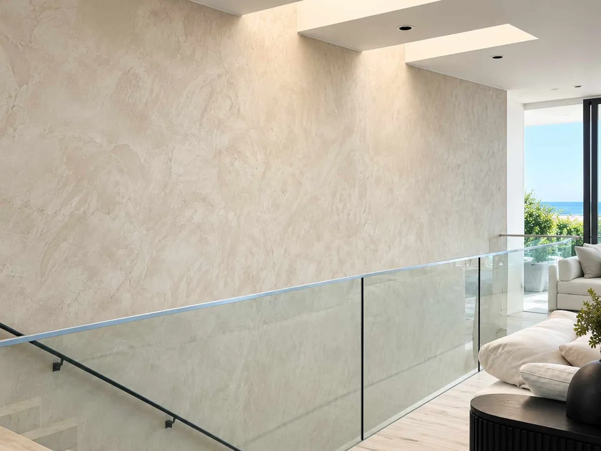 Tall landing wall in warm cream Venetian plaster with soft stone movement above a glass railing, ocean view beyond