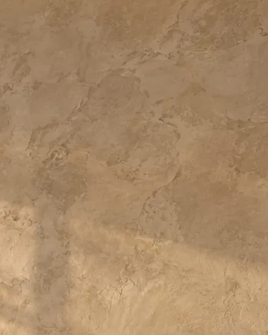 Close-up of sand-colored Marmorino plaster on a fireplace wall, with soft trowel marks and window light falling across the matte surface