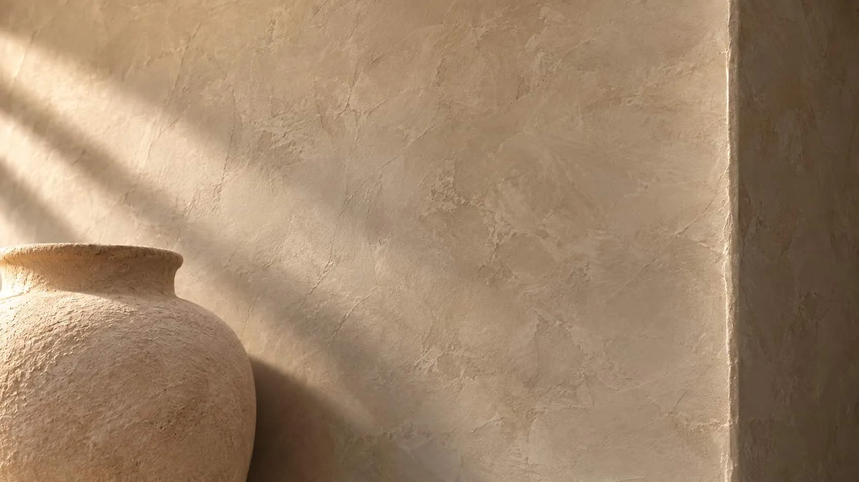 Warm beige Roman clay wall with soft trowel movement, a clay vase and window shadows
