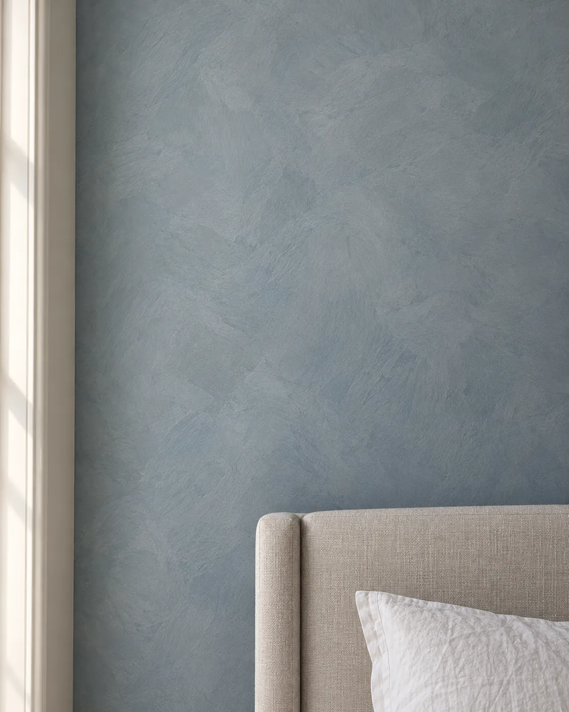 Close-up of dusty blue-gray limewash above a linen headboard, showing crisscross brush strokes and soft cloudy shifts