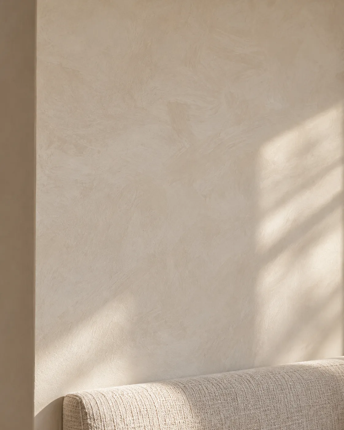 Close-up of pale mushroom limewash above a linen banquette, with loose brush sweeps and window light on the chalky surface
