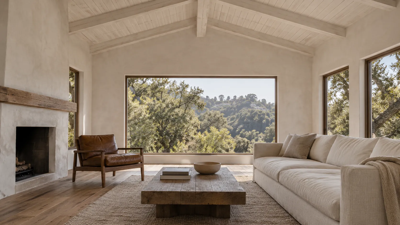 Living room with oyster white limewash walls, a whitewashed beamed ceiling, a plaster fireplace with an old wood mantel and a large window over an oak canyon