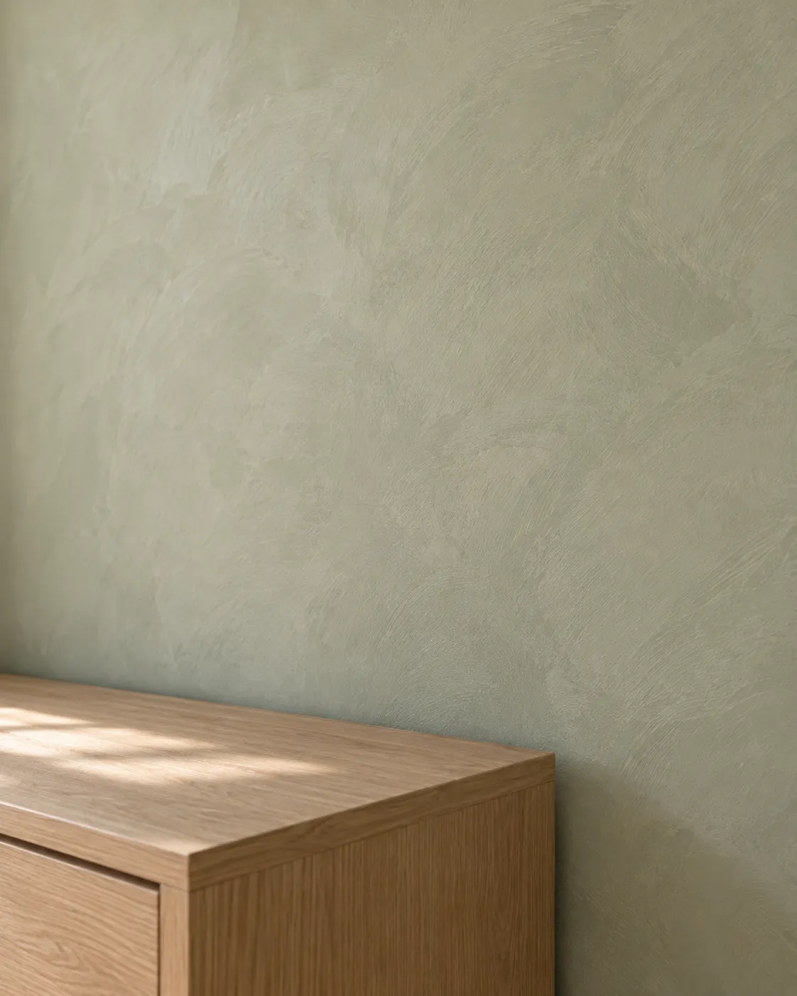 Close-up of soft sage limewash above an oak dresser, showing crisscross brush strokes and a flat chalky finish