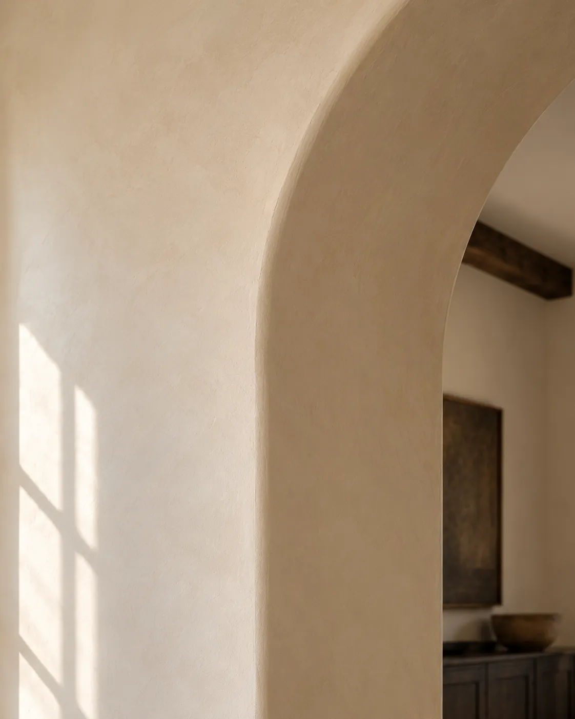 Close-up of warm cream Roman clay wrapping the rounded edge of an arched doorway, with window light on the matte surface