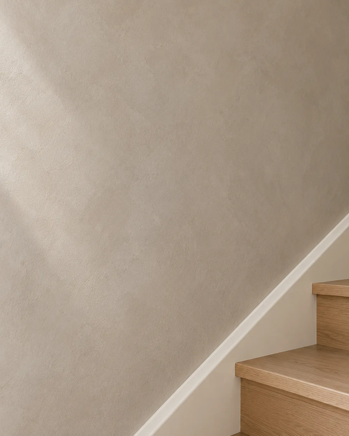 Close-up of greige Roman clay on a stair wall above white oak treads, with soft knife passes and a crisp painted skirt board