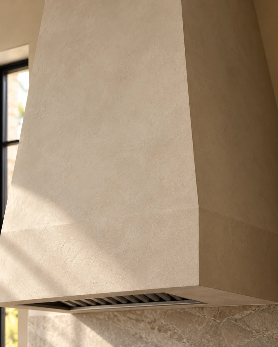 Close-up of a range hood in warm putty Roman clay, showing a matte velvety surface, soft knife marks and crisp plastered edges