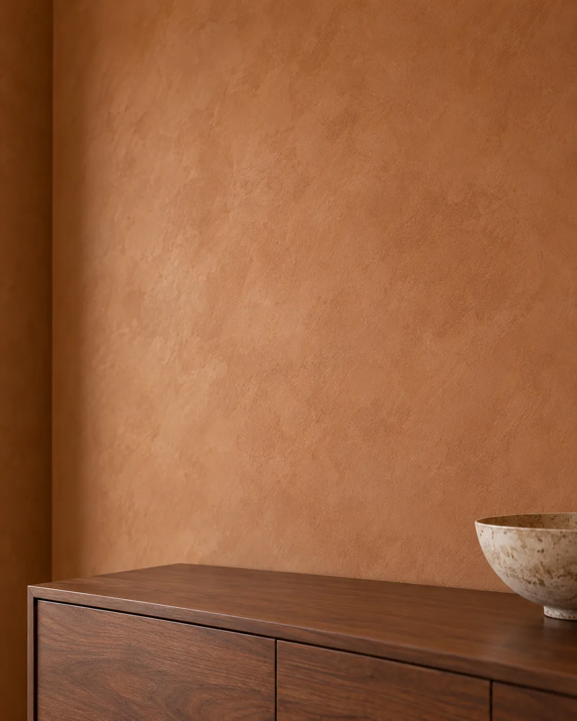 Close-up of warm saddle-brown Roman clay above a walnut credenza with a stone bowl, showing soft cloudy shifts in tone