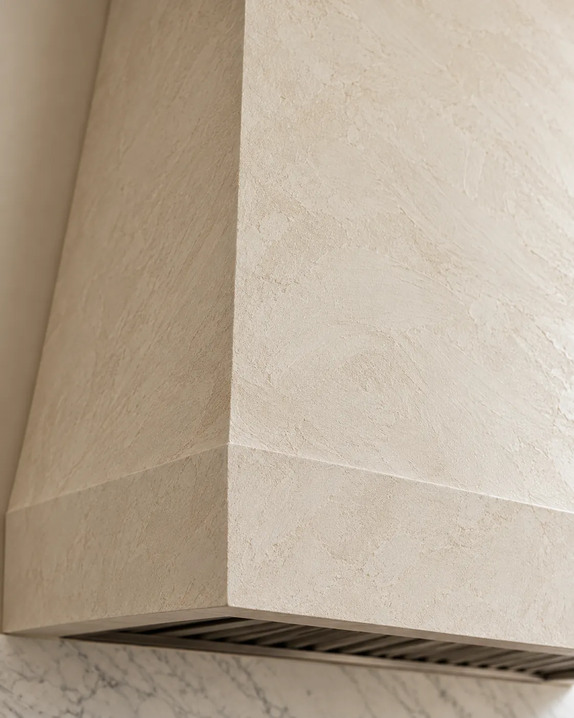 Close-up of a range hood corner in warm white Marmorino plaster, showing fine matte grain, soft trowel marks and a crisp plastered edge