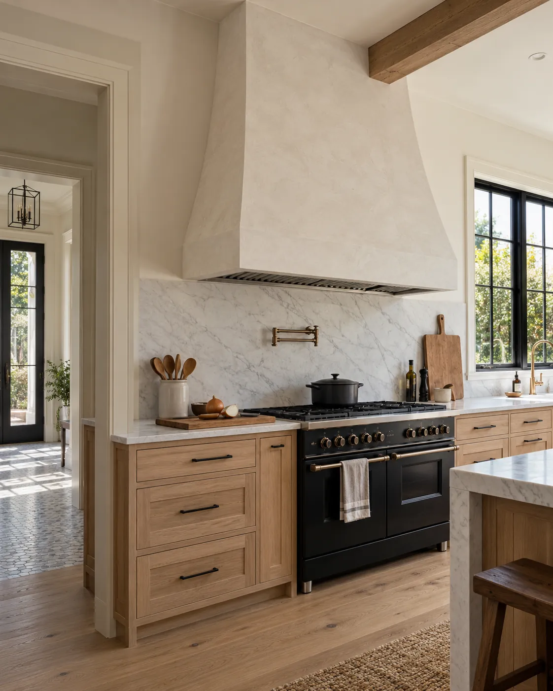 Kitchen with a tapered range hood in warm white Marmorino plaster above a marble slab backsplash, white oak cabinets and a black range