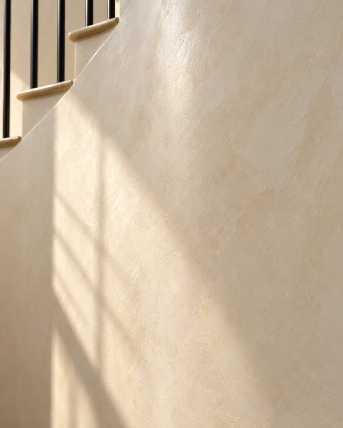 Close-up of ivory polished Venetian plaster on a curved stair wall, with soft cloudy veils and window light falling across it